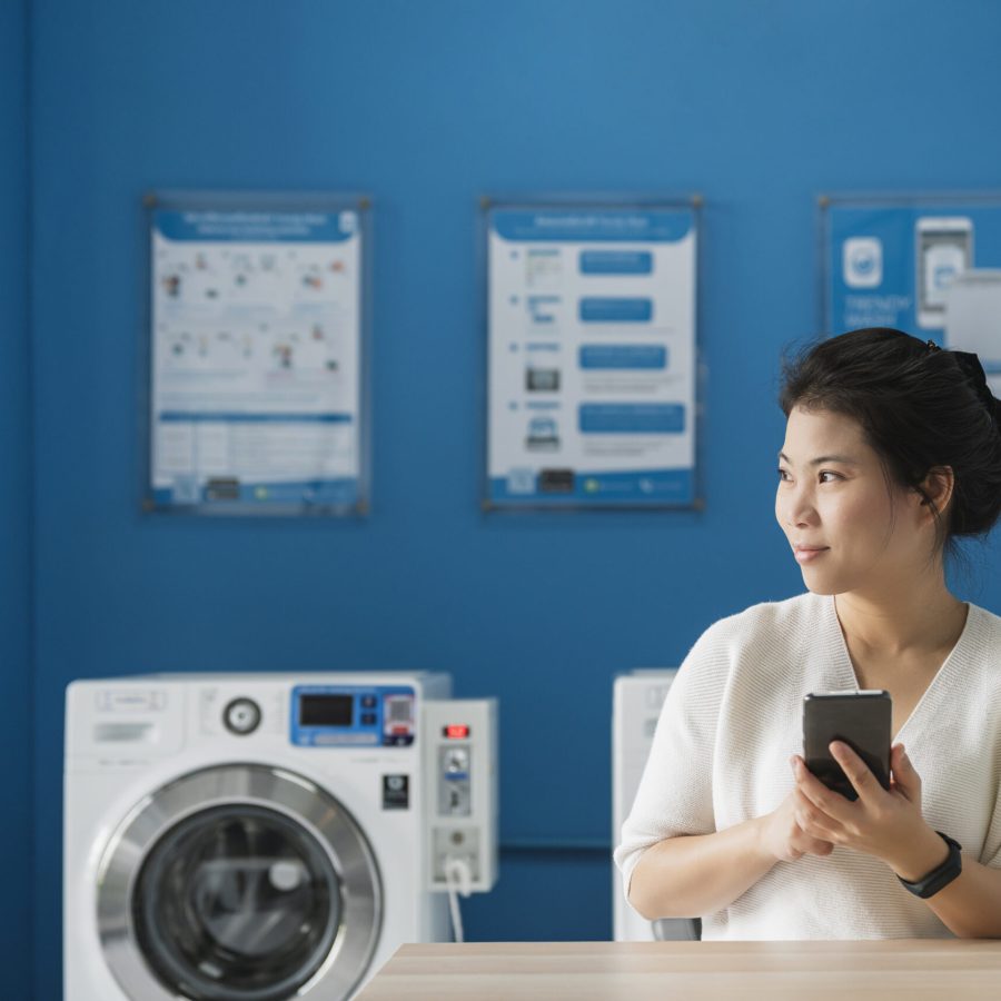portrait asian female hand use smartphone to check schedule of washing queue in blue color interior laundry shop in condoiminuim city lifestyle